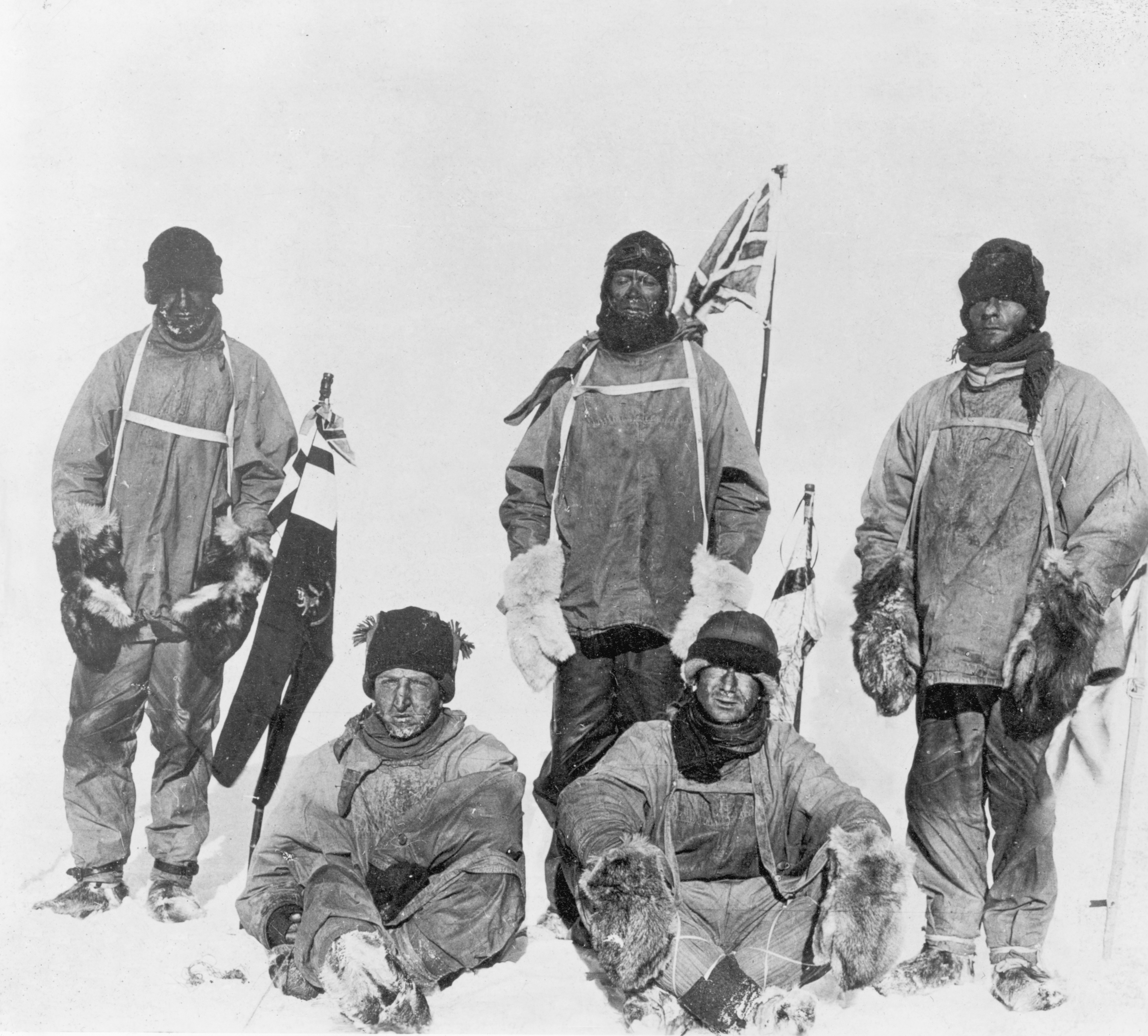 Black and white photo of five stoic-looking men in the snow; only their faces are exposed. Three are standing up and two are sitting in front.