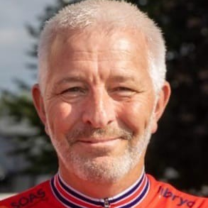 male with light grey hair and beard wearing red top