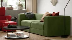 a modern green sofa sits in a living room, alongside a red armchair and a circular black coffee table.