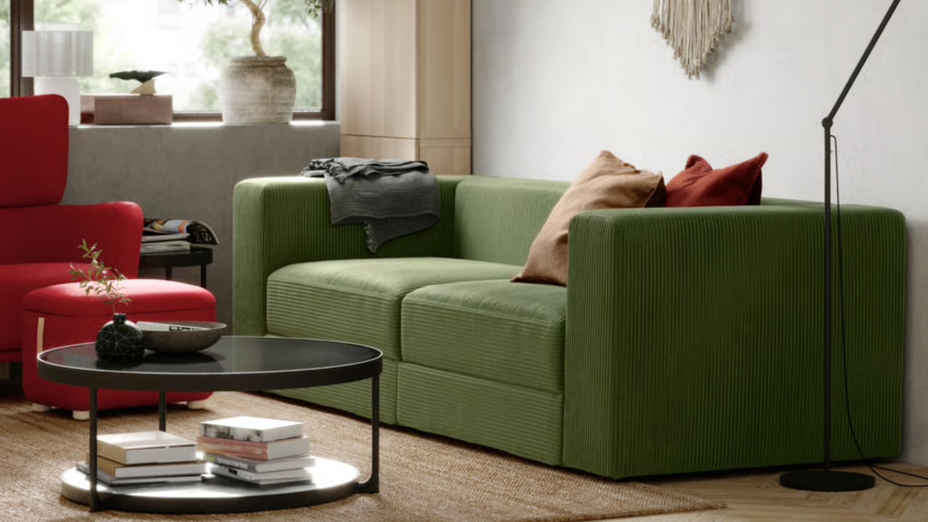 a modern green sofa sits in a living room, alongside a red armchair and a circular black coffee table.