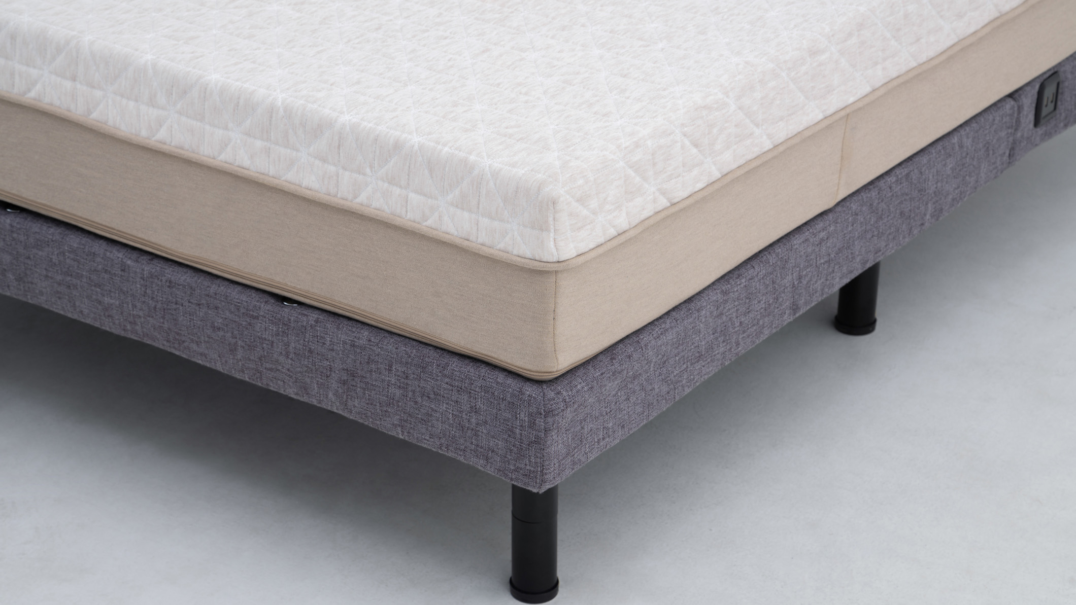 A corner of a mattress on a grey box spring