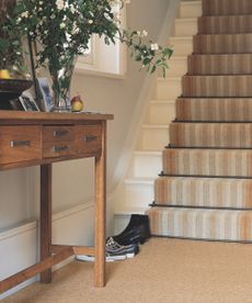 Staircase with carpet runner behind side table with fruit bowl, flower bouquet with vase, and portrait framed picture. (1)