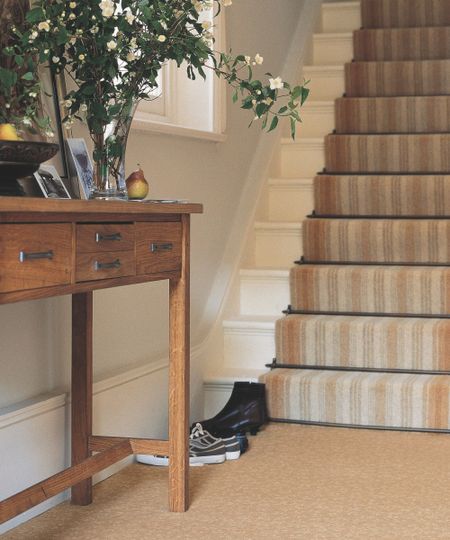 Staircase with carpet runner behind side table with fruit bowl, flower bouquet with vase, and portrait framed picture. (1)