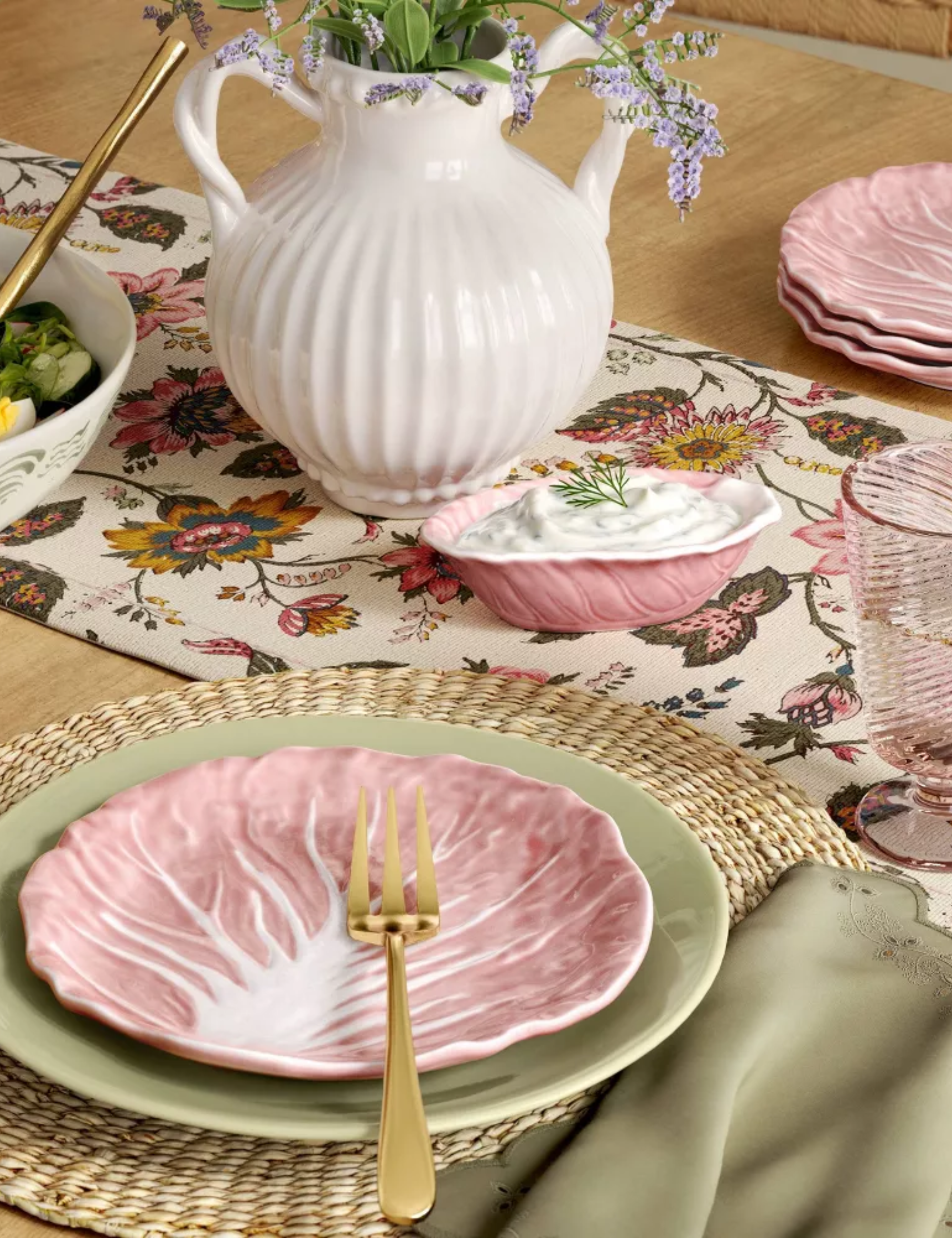 Spring tablescape featuring dinnerware in pastel green and pink hues, accented by woven plate chargers and golden flatware