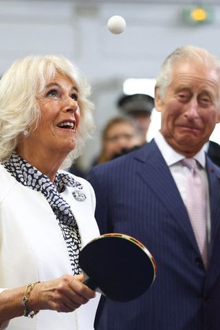 Queen Camilla playing ping pong as King Charles looks on
