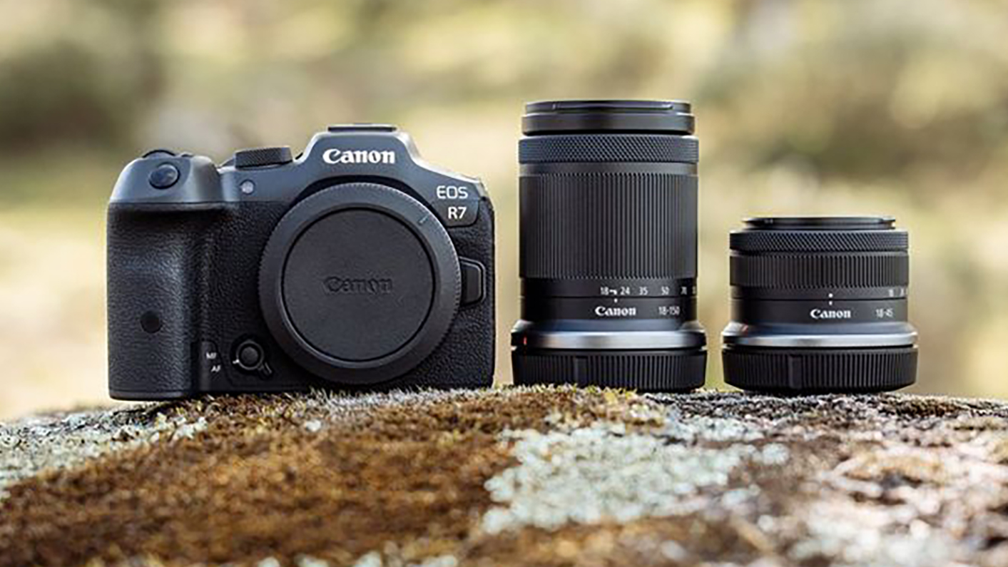 The Canon EOS R7 on a rock next to two lenses