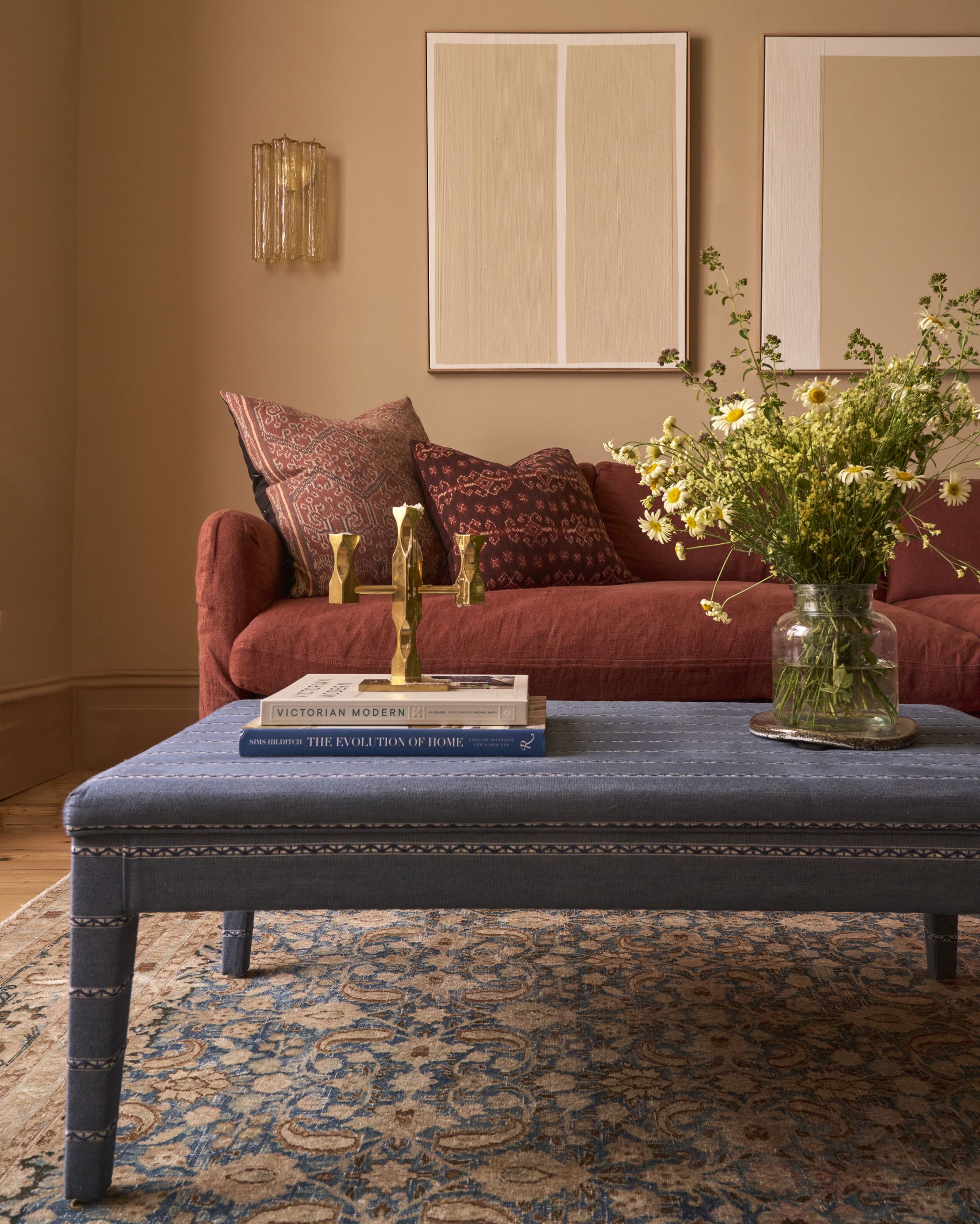 Image of a warm, beige living room with a red sofa, a blue patterned sofa, and a blue upholstered ottoman. 
