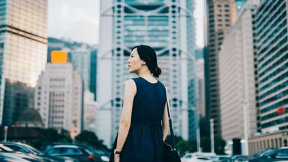 Successful young businesswoman looking away with confidence standing against urban cityscape