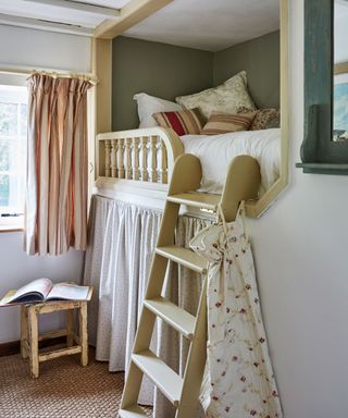 Country, period bedroom with wooden bunkbed, dressed with blankets and cushions, curtains below bunk bed, beamed ceiling
