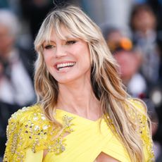 Heidi Klum smiles and looks away from the camera in a yellow dress