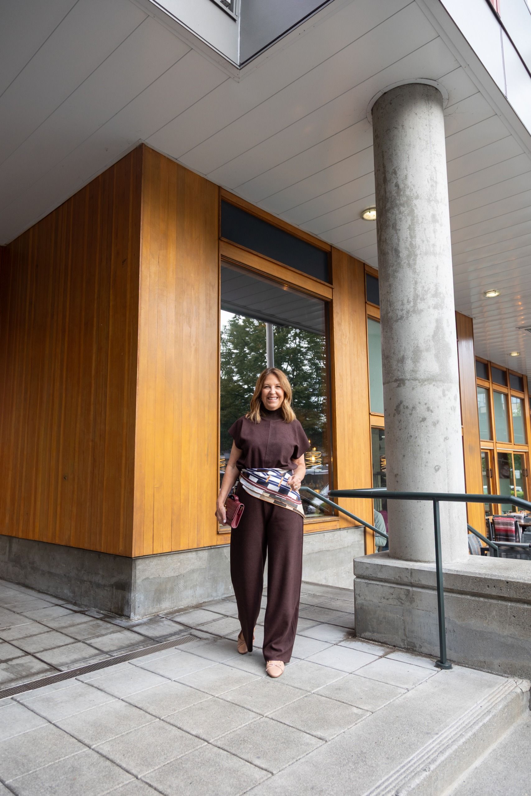 Sandy Koszarek wearing a brown blouse and brown trousers with a patterned scarf tied around her waist.
