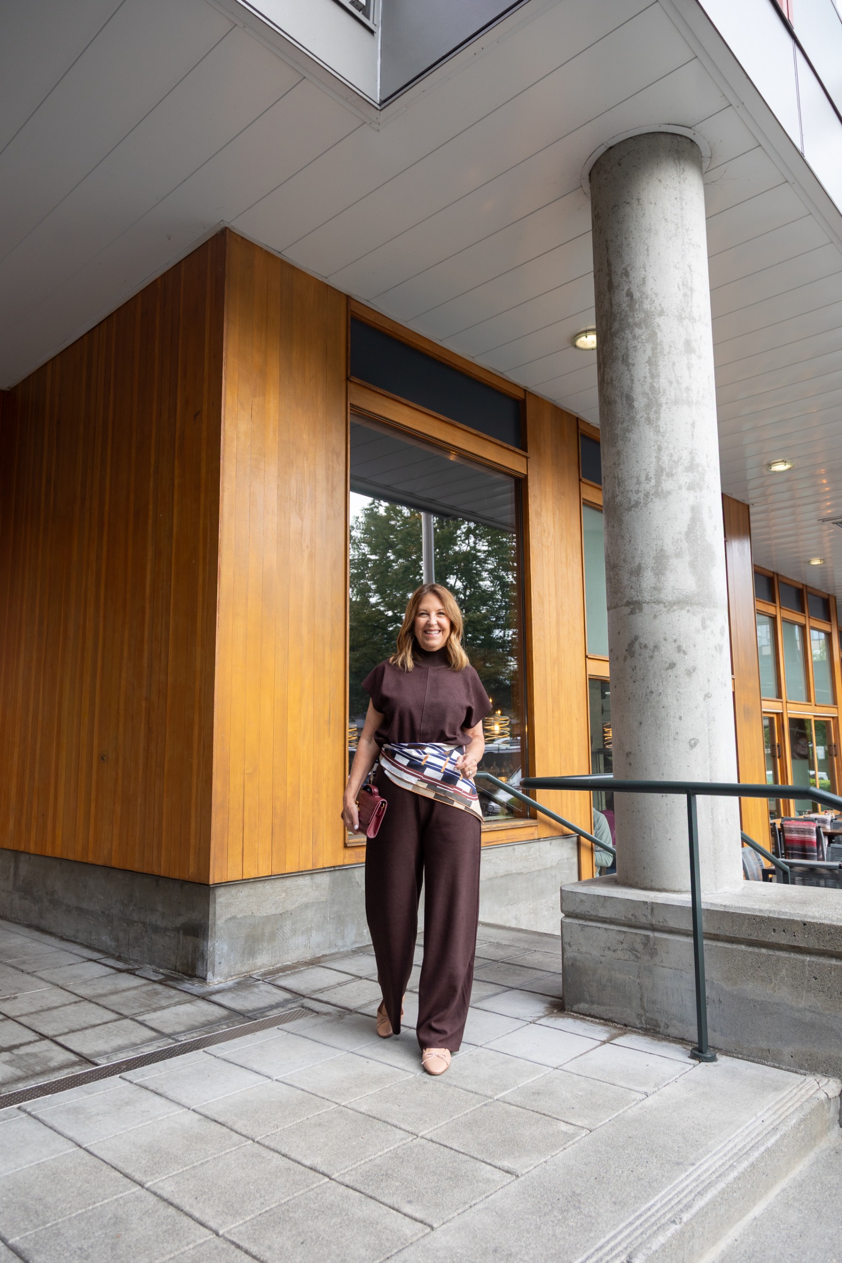 Sandy Koszarek wearing a brown blouse and brown trousers with a patterned scarf tied around her waist.