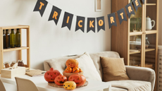 A beige living room with a halloween banner and pile of pumpkins on the table