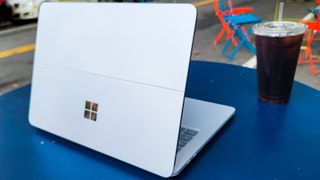 Surface Laptop Studio from behind, on a blue table next to iced coffee