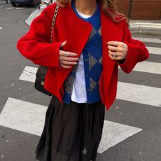 Close-up image of influencer @rebeccaferrazwyatt wearing a blue argyle cardigan over a white t-shirt with a black skirt and red jacket.