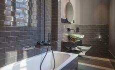 Bathroom featuring grey, tiled walls and floor, black fixtures and a decorated sink bowl