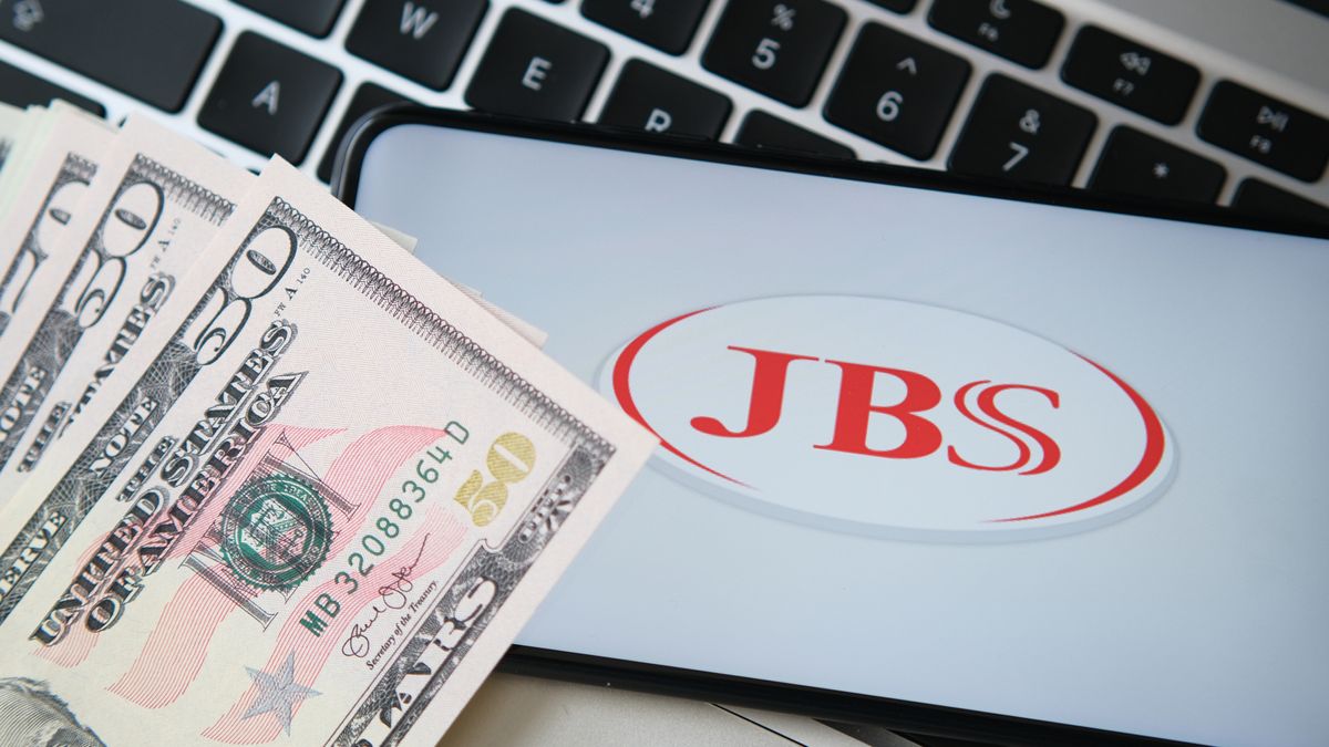 JBS meat producer logo seen on the smartphone screen with blurred money and laptop keyboard on the background