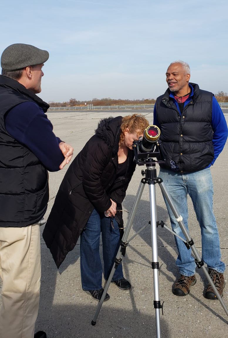 Former journalist Martin Evans (right) chats with two fellow guests of the Amateur Astronomers Association (AAA) gathering on Monday, Nov. 11, 2019, in Floyd Bennett Field, New York. Peering through the Orion EZ Finder II telescope is a mother who brought her children to the viewing event; standing to the left is amateur astronomer Stephen Lieber. 