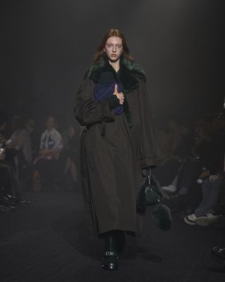 Woman on Burberry runway in trench coat holding hot water bottle