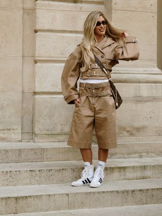 woman wearing a tan outfit and boxing-style sneakers.