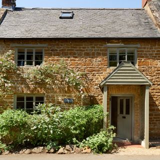 Front exterior of a country cottage with green painted window frames and front door with a small porch over