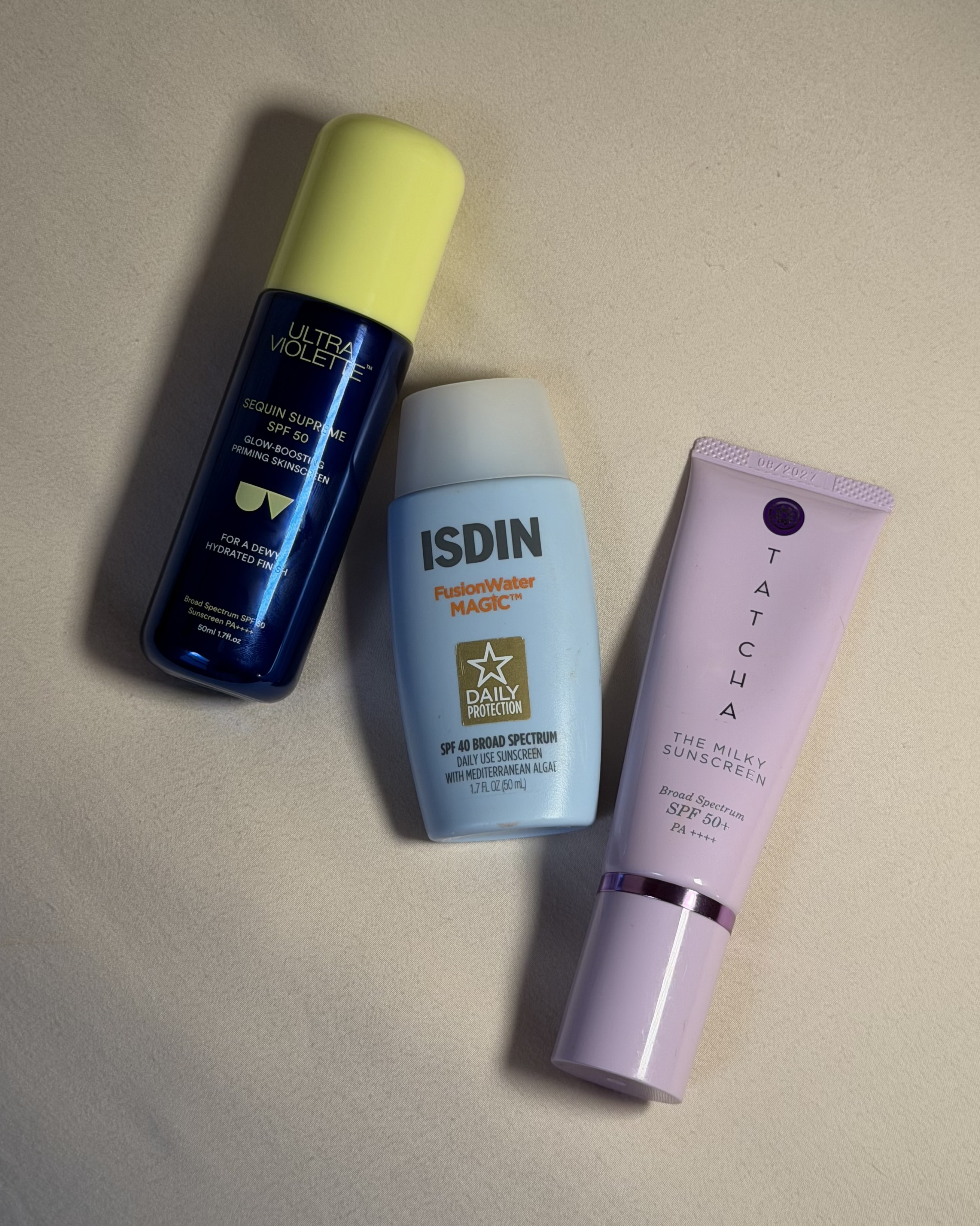 Bottles of Ultra Violette, Isdin, and Tacha sunscreens lying on a table.