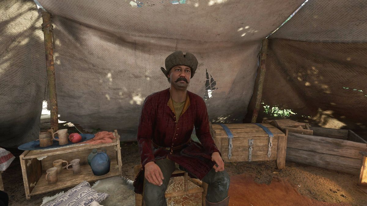 Kingdom Come Deliverance 2 Marika location - A man sitting down inside a tent, surrounded by clutter.