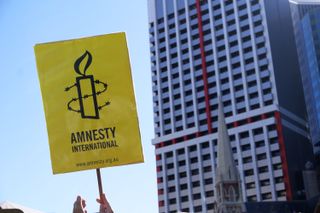 A sign bearing the Amnesty International logo is held up in front of a skyscraper
