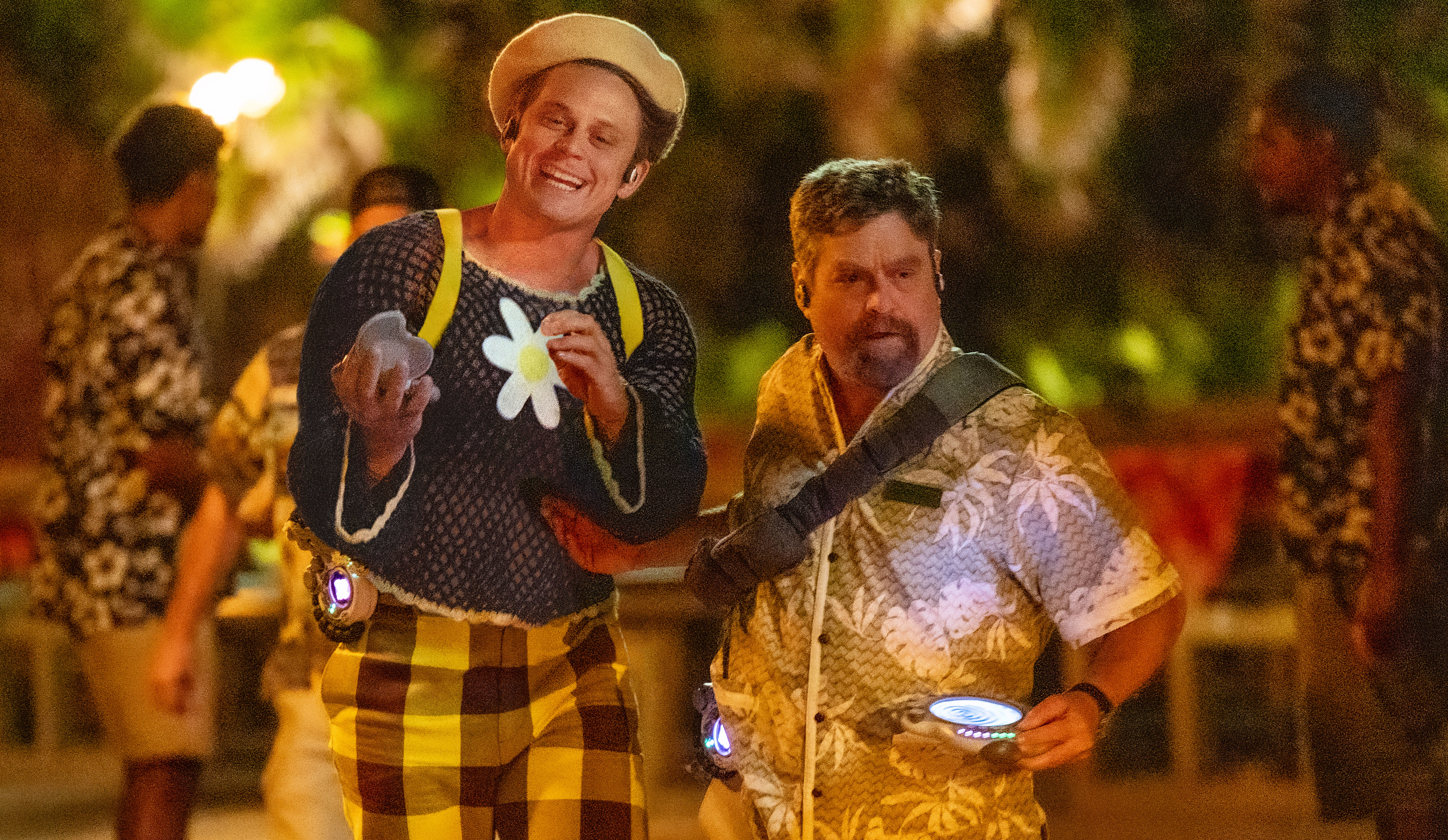 Billy Magnussen and Zack Galifianakis walk through a luau in their human disguises in Lilo and Stitch.