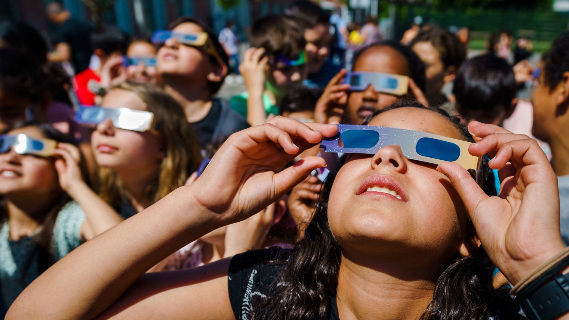 Children wearing solar eclipse glasses look at the sun