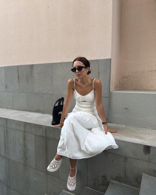 Debora Rosa mengenakan gaun midi putih dengan sepatu flat Hvóya rajutan putih.