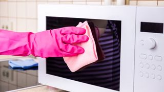 How to clean a microwave: Woman wearing pink glove wiping microwave door
