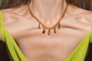 A close up of a woman's neckline wearing a gold necklace with the words 'Amour'