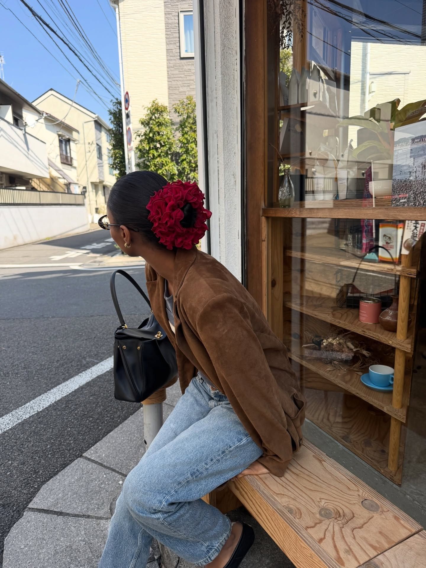 rayan xasan wears a brown jacket, jeans and an undone handbag