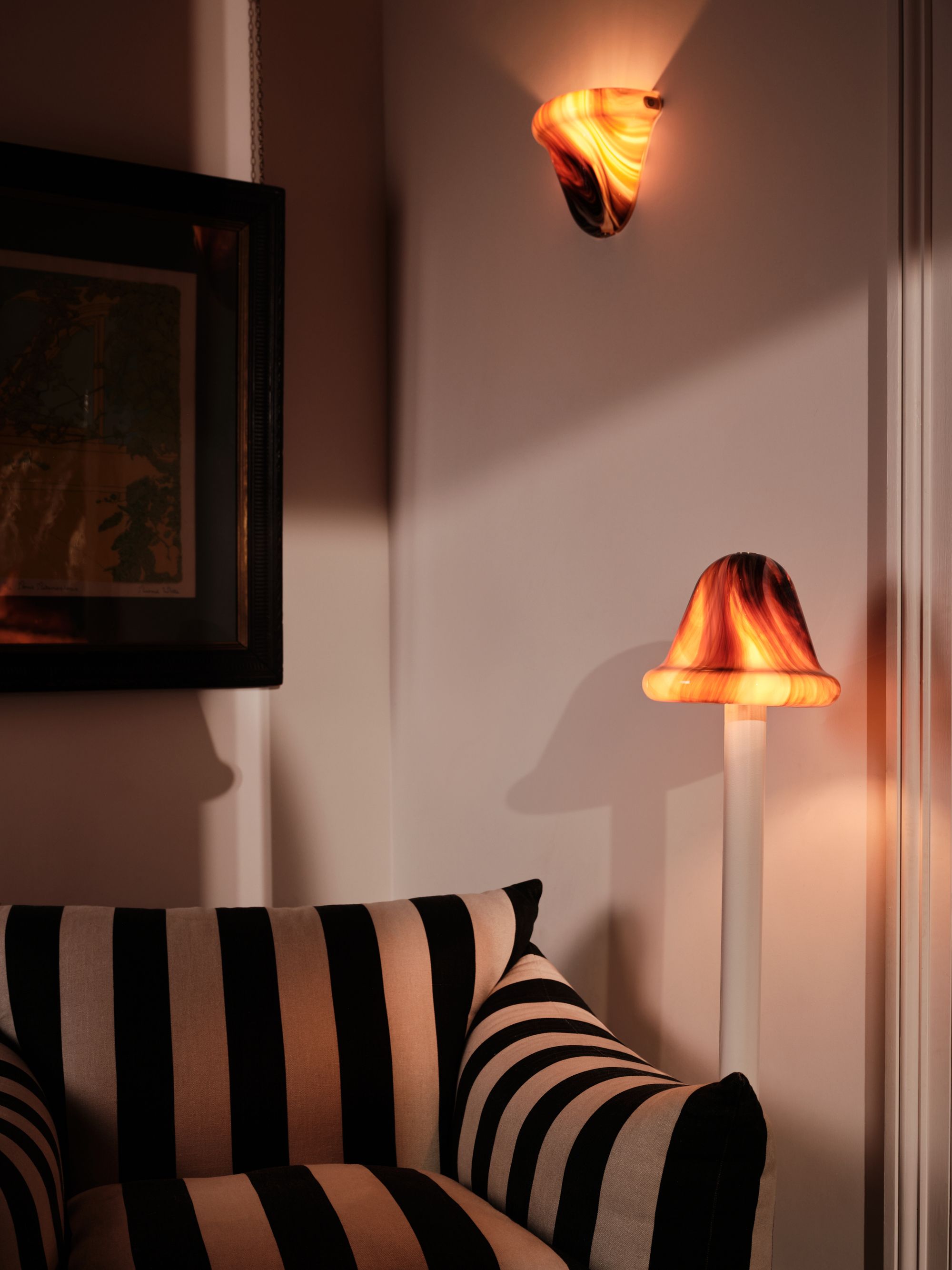 Image of an overstuffed black and white striped side chair with a brown marble and white floor lamp beside it and a matching scone light hanging above.