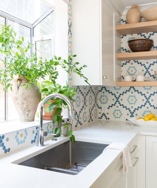 A white kitchen with blue and white patterned tiles, white countertop, and brushed metal sink