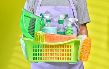 A person is holding a basket full of various cleaning products.