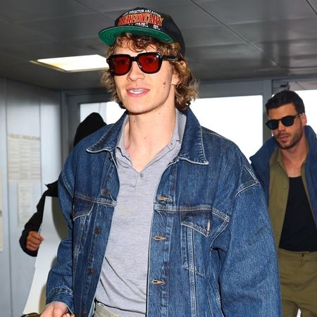 Connor Storrie wears a hat, red sunlgasses, a gray polo shirt, and a denim jacket.