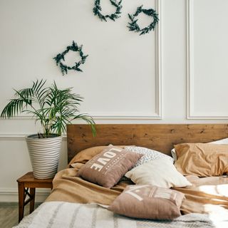 hygge bedroom with plants, wreaths, a wooden headboard, white walls, and peach-colored bedding