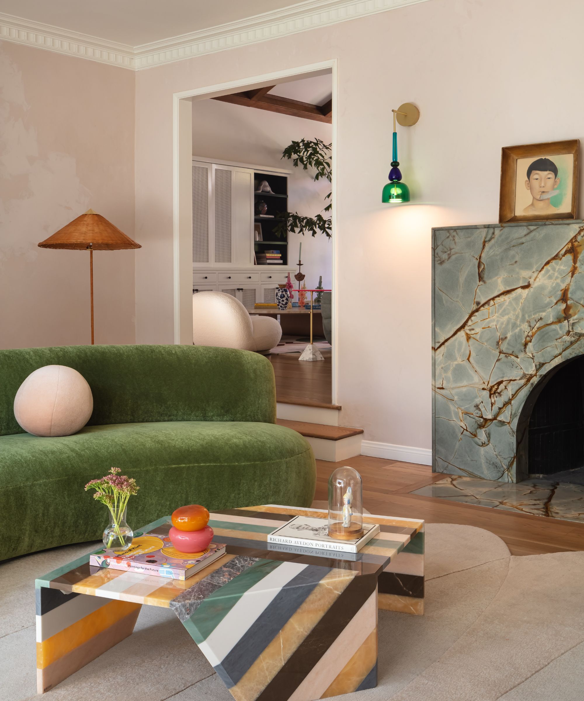 Creamy pink living room with marble fireplace and a velvet green sofa with striped stone coffee table