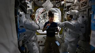 Three astronauts, two in spacesuits, test spacesuits for a spacewalk on the International Space Station