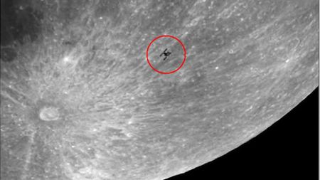 The silhouette of a space station is shown on the lunar surface surrounded by a red circle. A large crater is visible to its lower right, with bright lines emanating outwards.