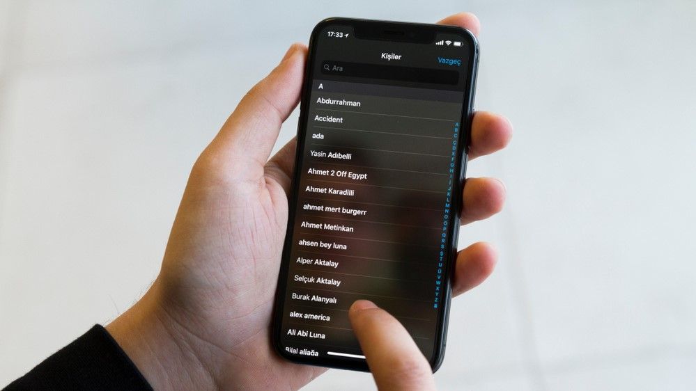 An iPhone with the Contacts app open, with the user scrolling through it with their finger