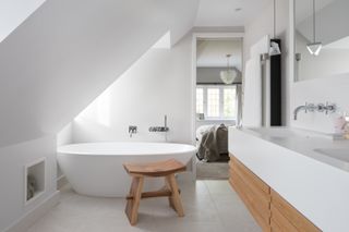 white bathroom, ensuite, loft, wall hanging double vanity, stool, white modern tub, white floor