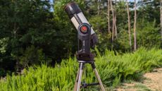 a black and white telescope in a field with trees behind it