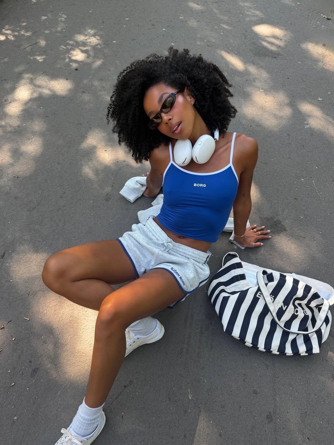 A woman with a curly hairstyle reclining on the pavement while wearing athletic clothing