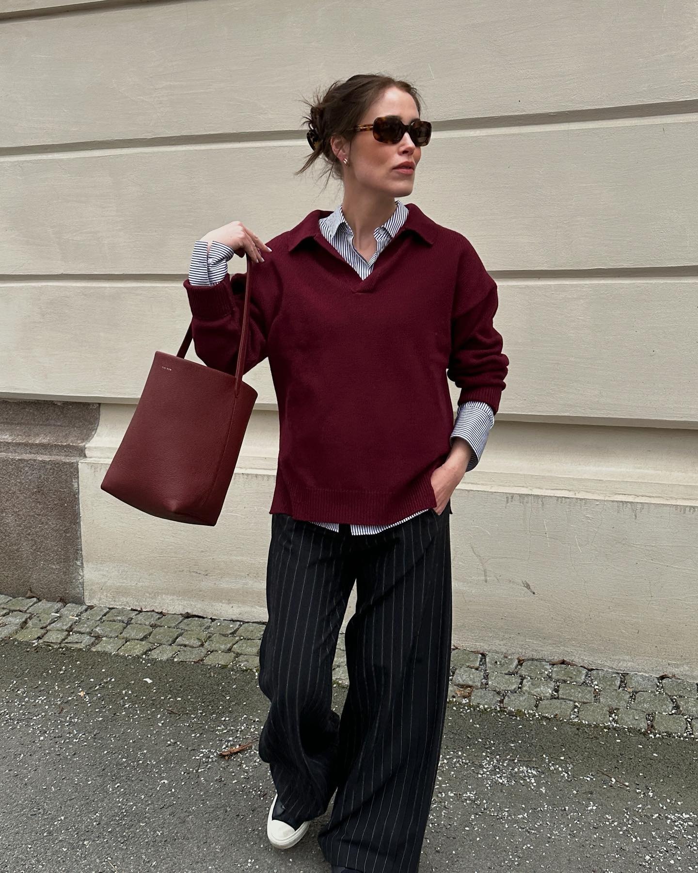 Woman wears burgundy jumper, striped shirt, striped trousers, burgundy bag