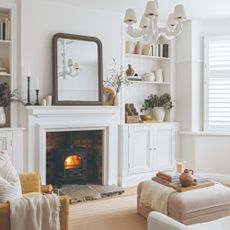 A white living room with a lit fireplace and a curved-edge mirror leaning on top of it