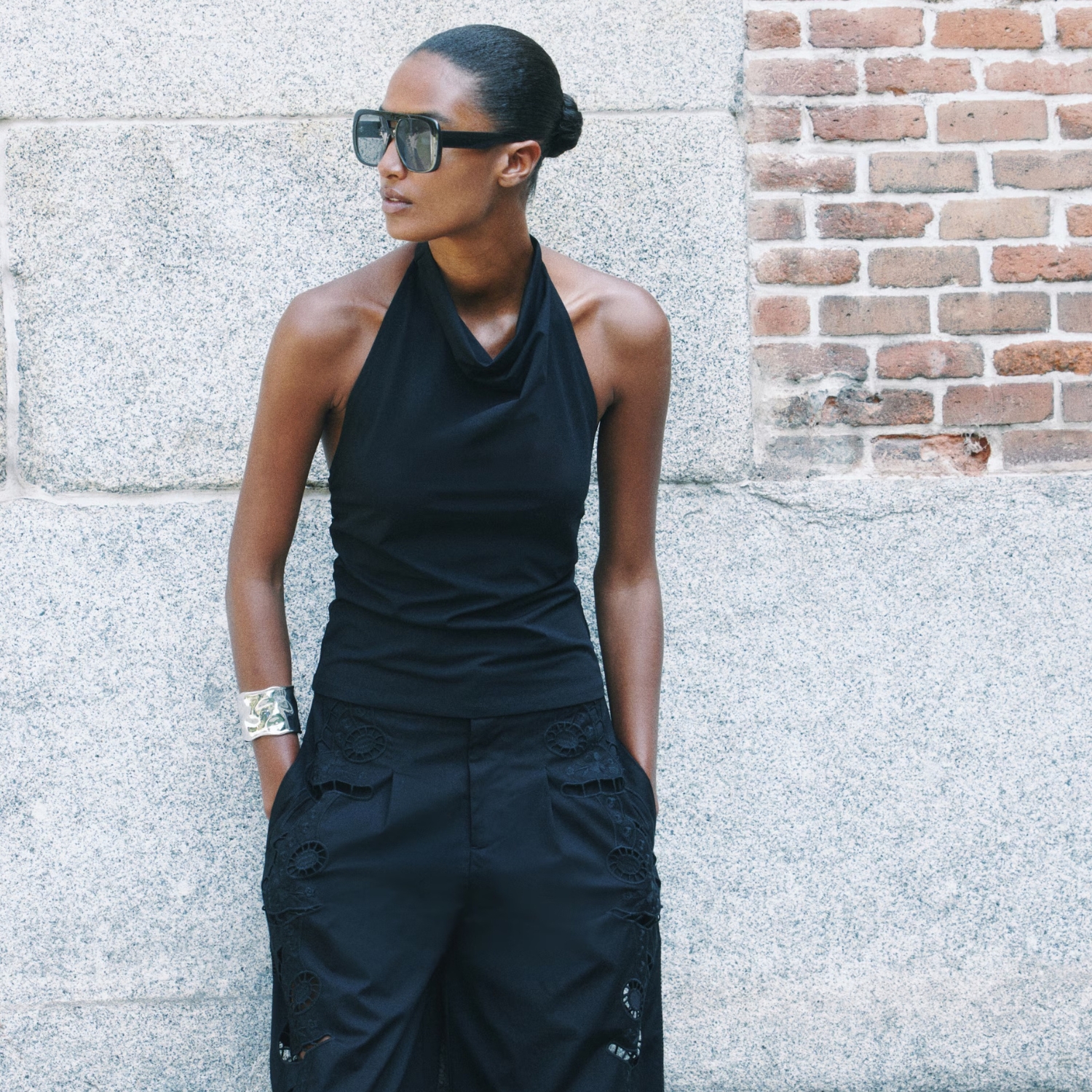 Model wearing a H&M black halterneck top and black broderie anglaise trousers, plus blue aviator sunglasses and a silver bracelet.