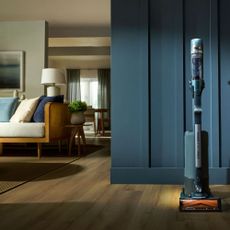 Teal-coloured shark vacuum cleaner in front of teal panelling in a living room
